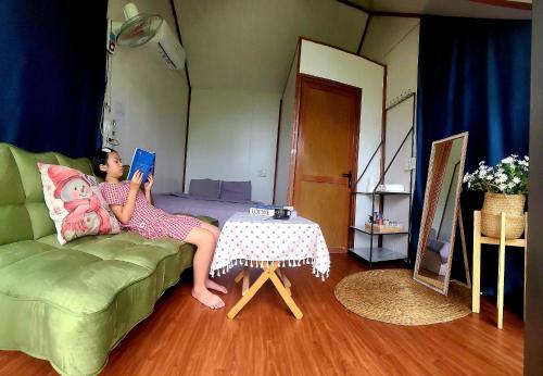 a woman sitting on a couch reading a book at Homstay Mimosa Mộc Châu in Mộc Châu