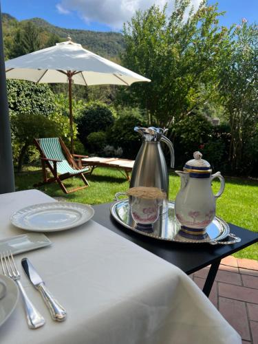 a table with a tea kettle and plates and an umbrella at Antico Borgo Sanda Lago Maggiore in Casalzuigno