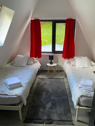two beds in a room with a window with red curtains at Cabana A Morarului in Teiuş