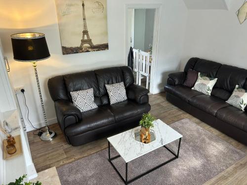 a living room with a black leather couch and a table at Ty Abertawe in Cockett