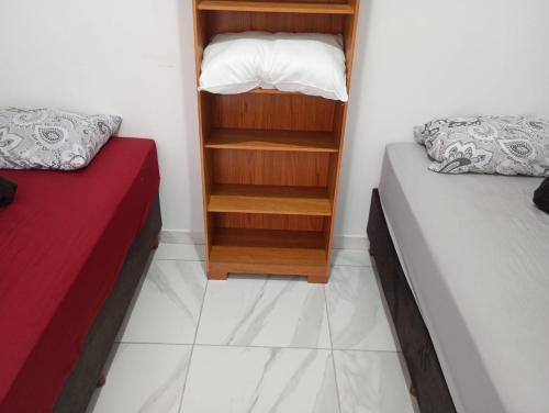 a small room with two beds and a book shelf at Espaço Marques com ar in Porto Seguro