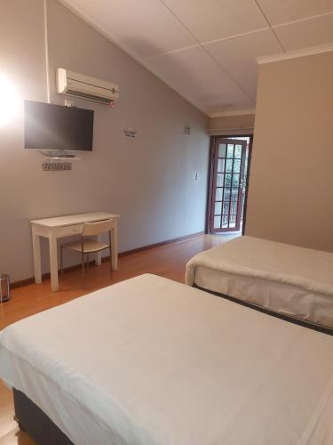 a room with two beds and a table and a tv at The Comfort Zone - Mthatha in Mthatha