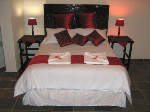 a bedroom with a bed with red and white pillows at Ukarimu Guest House in Klerksdorp