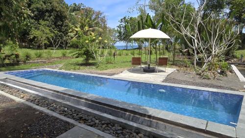 a swimming pool with an umbrella next to a yard at Melaya Cabanas in Candikesuma