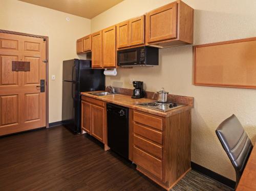a small kitchen with wooden cabinets and a black refrigerator at Candlewood Suites St. Robert by IHG in Saint Robert