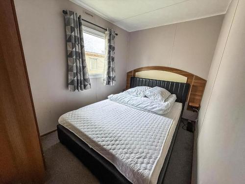 a small bedroom with a bed with white sheets and a window at Superb 8 Berth Caravan At Highfield Grange Ref 26706Wr in Clacton-on-Sea