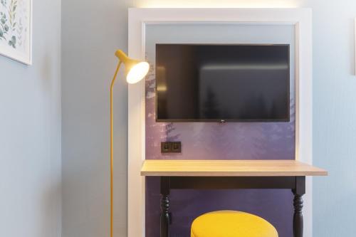 a tv on a wall next to a table with a yellow chair at Garner Hotel Essen - Messe by IHG in Essen