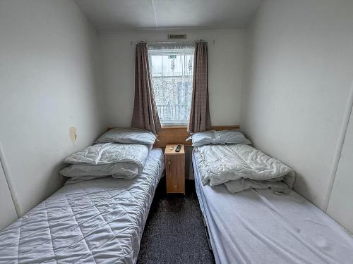 Dos camas en una habitación pequeña con ventana. en 6 Berth Staycation Caravan Nearby Clacton-On-Sea In Essex Ref 26254E, en Clacton-on-Sea