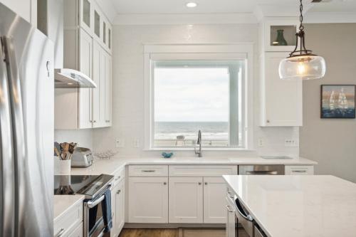 a kitchen with white cabinets and a window with the ocean at 207 E Arctic - Seahorsing Around - Oceanfront - 3 Bedrooms in Folly Beach