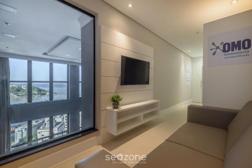 a living room with a large window and a tv at MHFA - Studios em Prédio Luxuoso com Vista Mar in Itapema