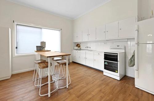 a kitchen with white cabinets and a table and stools at Ocean Road Retreat in Peterborough