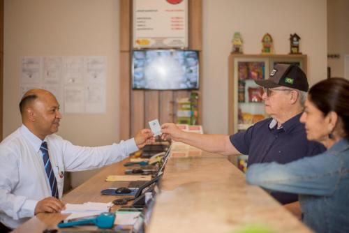 a man handing a card to a customer at a counter at Hotel Tropical Garden in Primavera do Leste