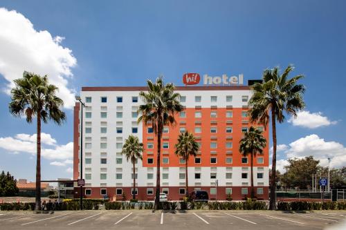 a hotel with palm trees in front of a parking lot at Hotel Hi! Zapopan in Guadalajara