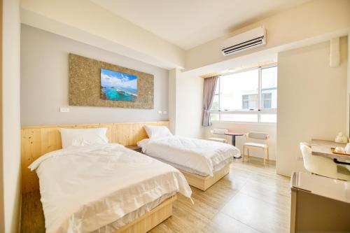 a bedroom with two beds and a table and a window at 看海季節&聽海約定精緻旅店 in Magong
