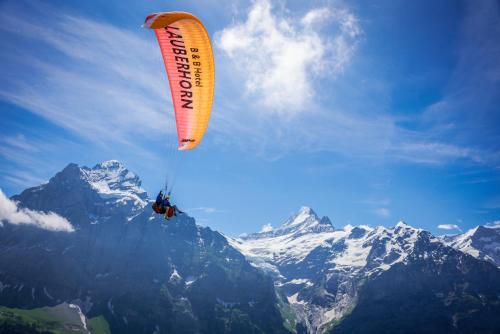 una persona en un paracaídas volando sobre una montaña en Hotel Lauberhorn - Home for Outdoor Activities, en Grindelwald