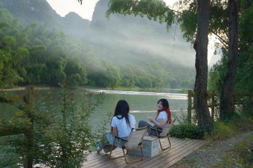 two women sitting on a wooden deck near a lake at The Apsara Lodge-Airport or TS Free pick-up over 3 nights in Yangshuo