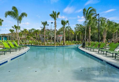 a swimming pool at a resort with green chairs and palm trees at Stunning Townhouses 5 Minutes away Disney! in Kissimmee
