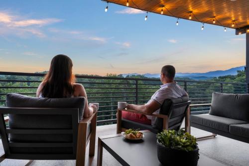 a man and a woman sitting on a balcony watching the sunset at Modern Rooftop Mtn Views, Hot Tub, Indoor Pool, Near Dollywood & PS5 in Pigeon Forge