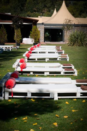 a row of white benches with red umbrellas in the grass at Hotel Balneario Valle del Jerte in Valdastillas
