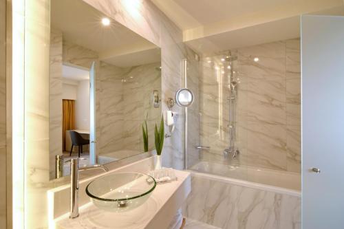 uma casa de banho com um lavatório de vidro e uma banheira em Athens Avenue Hotel em Atenas