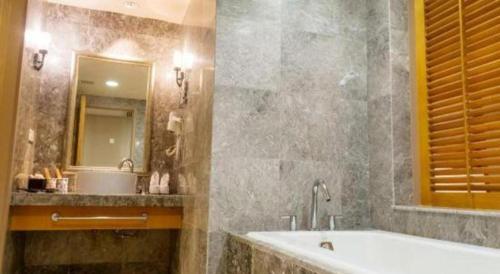 a bathroom with a tub and a sink and a mirror at Ocean Spring Metropark Hotel Zhuhai in Zhuhai