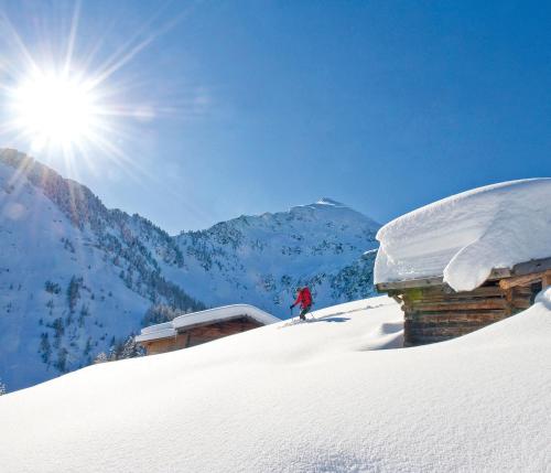 a person on skis in the snow next to a cabin at Hotel Alphof Alpbach in Alpbach