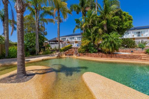 a swimming pool with a palm tree in front of a building at The Quarters, an Ascend Collection Hotel in Wamberal