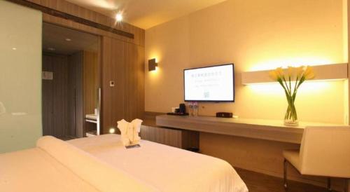a hotel room with a bed and a desk with a tv at Jinjiang Metropolo Hotel - Qingdao Chengyang District Government in Qingdao