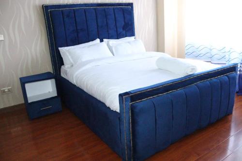 a large bed with a blue headboard and a night stand at modern executive three bedroom apartment which features a swimming pool, state of the art fully equipped gym and all modern unmatched luxurious facilities which offfers luxury lifestyle in Nairobi