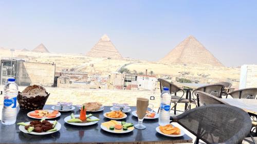 a table with plates of food and the pyramids at Hi pyramids view in Banī Ghālib