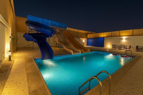 a swimming pool with a slide in a hotel at night at Tamyoz Aqama for Serviced Apartments in Hail