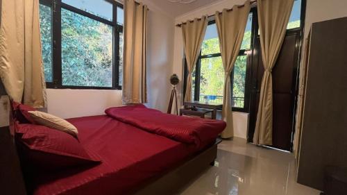 a bedroom with a bed with red sheets and windows at riverview villa in Bīr