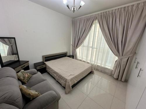 a bedroom with a bed and a couch and a window at Big flat 3 bedrooms, in floor 15 full service in Sharjah