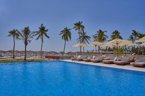 a swimming pool with chairs and umbrellas and palm trees at The Club by Fanar in Salalah