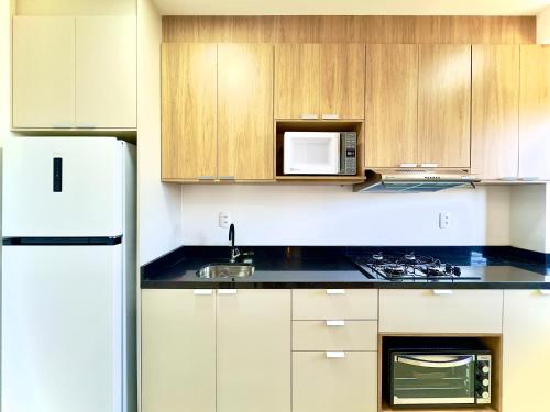 a kitchen with a white refrigerator and wooden cabinets at Apto 2 Quartos PISCINA Churrasqueira Wi-Fi Ar Condicionado Cozinha Complata Vaga de Garagem 400m PRAIA Ideal para Famílias ou Amigos Reserve Agora in Piçarras
