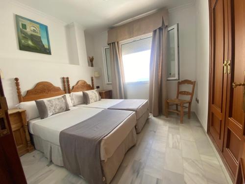 a bedroom with two beds and a chair and a window at Hotel La Española in Chipiona