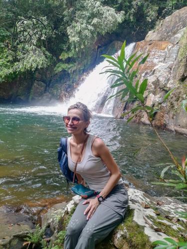 a woman sitting on a rock next to a river at Sinharaja Forest Sanctuary in Deniyaya