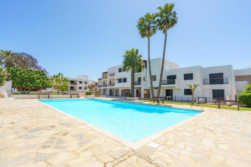 a swimming pool in front of a building with palm trees at Cozy Apartment in Kapparis #80 in Paralimni
