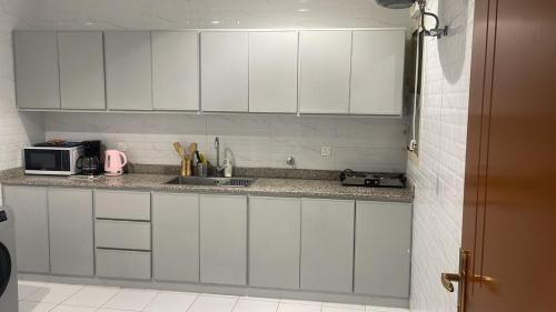 a white kitchen with a sink and a microwave at شقة بغرفتي نوم بالقرب من المطار in Tabuk