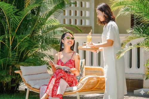a woman in a red dress sitting on a chair with a waitress at Én Retreat Hoi An in Hoi An