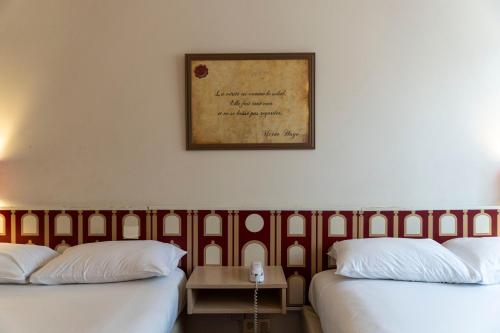 two beds in a room with a picture on the wall at Hotel Ours Blanc - Victor Hugo in Toulouse