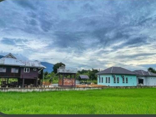 a group of houses and a field with a cloudy sky at D' Bamboo Madu Homestay in Yan