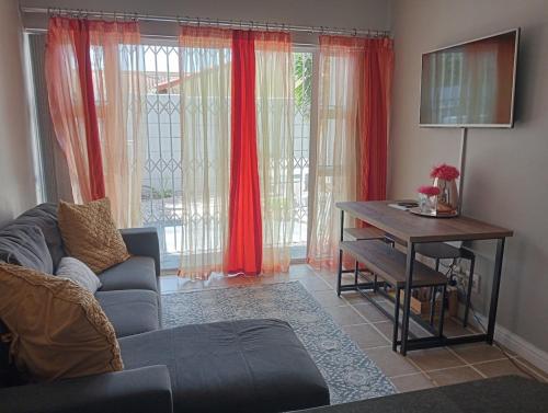 a living room with a couch and a table and red curtains at The Sands Ground-floor apartment in Blouberg in Cape Town