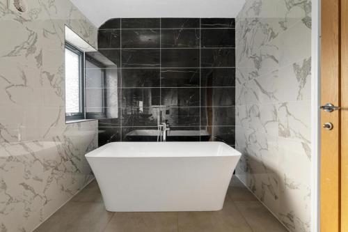 a white bath tub in a bathroom with black tiles at Luxurious Relaxing 5 Bed House for great comfort in Lutterworth