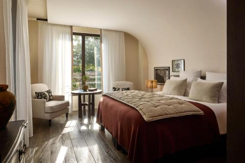 a bedroom with a bed and a chair and a window at L'Isle de Leos Hotel & Spa - MGallery Collection in LʼIsle-sur-la-Sorgue