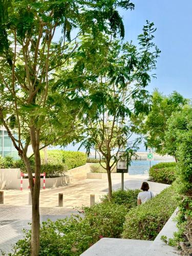 a person sitting on a bench in a park with trees at Al Mouj Marina Apartment with Pool & Beach Access in Ḩayl Āl ‘Umayr