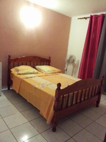 a bedroom with a wooden bed with a red curtain at F3 Meublé de Charme dans un écrin naturel en bas de Villa in Pointe-Noire