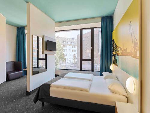 a bedroom with a bed and a large window at B&B HOTEL Münster Hafen in Münster