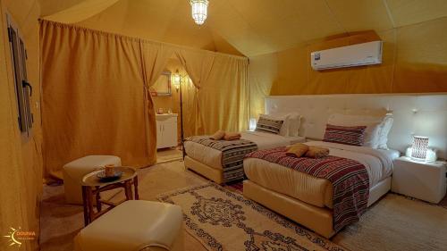 a bedroom with two beds and a chair and a table at Dounia Luxury Camp in Merzouga