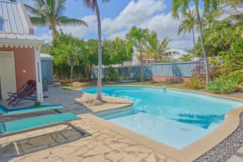 una piscina con palmeras y una casa en Le Jardin des Sables avec piscine - 10 voyageurs, en Saint-Paul
